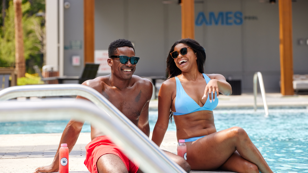 A woman and man resident sitting in the sun by the pool at The Ames